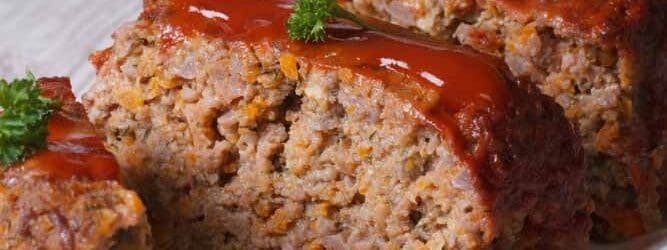 Meatloaf with ketchup closeup sliced on a white plate, vertical